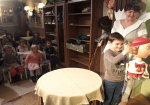 Aktorka na scenie stojąca przy stoliku oraz chłopiec trzymający pacynkę.